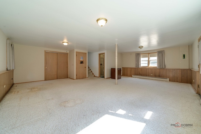 carpeted spare room featuring wooden walls and baseboard heating