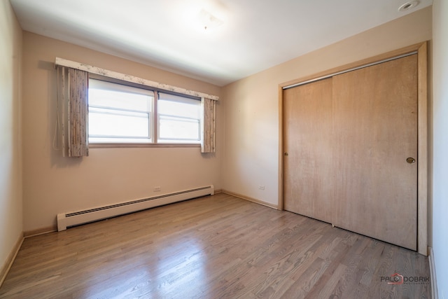 unfurnished bedroom featuring light wood-type flooring, baseboard heating, and a closet