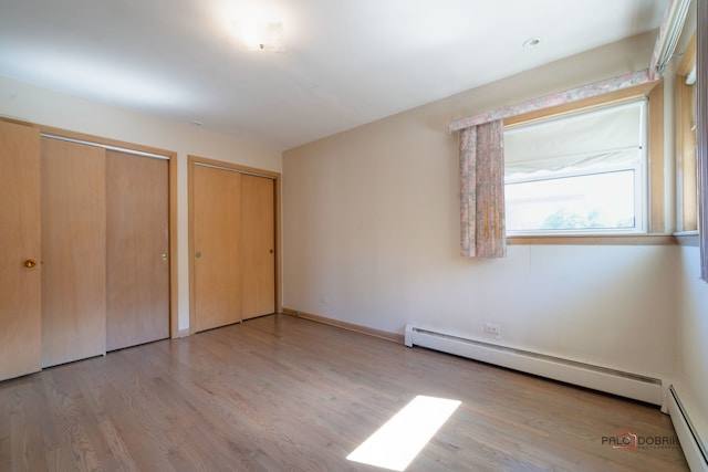 unfurnished bedroom featuring light hardwood / wood-style floors, multiple closets, and a baseboard radiator