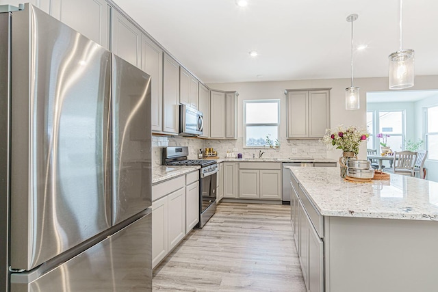 kitchen featuring decorative backsplash, a kitchen island, appliances with stainless steel finishes, decorative light fixtures, and gray cabinetry