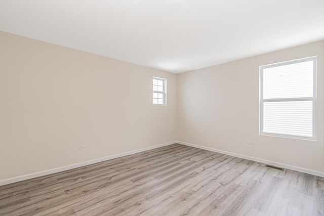 empty room featuring light wood-style flooring, visible vents, and baseboards