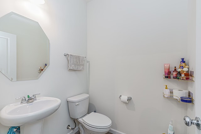 half bath with baseboards, a sink, and toilet