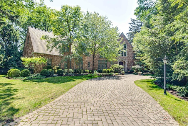 tudor house with brick siding, decorative driveway, and a front yard