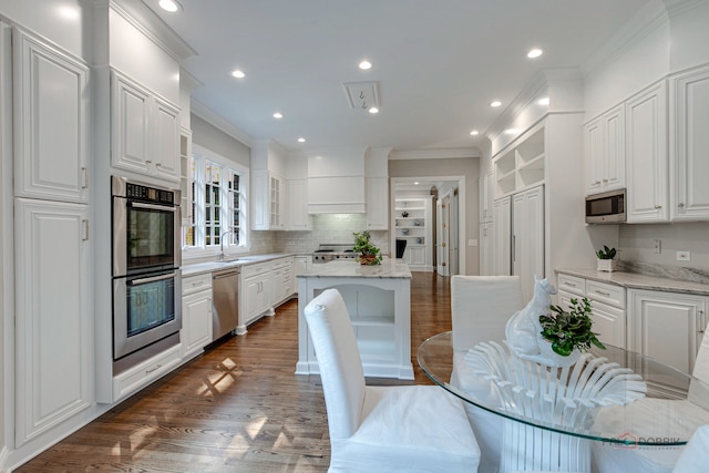 kitchen with stainless steel appliances, white cabinets, light stone counters, dark hardwood / wood-style floors, and a kitchen island