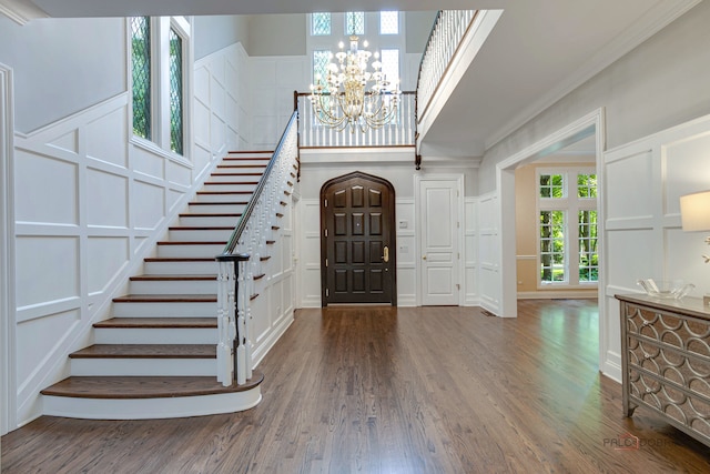 entryway featuring ornamental molding, hardwood / wood-style flooring, a notable chandelier, and a towering ceiling