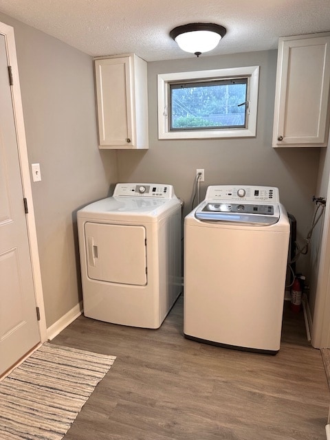 laundry room with separate washer and dryer, light hardwood / wood-style floors, cabinets, and a textured ceiling