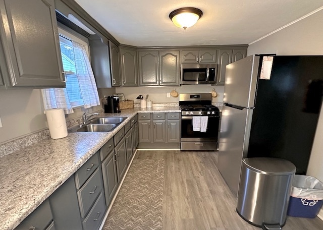 kitchen featuring appliances with stainless steel finishes, light hardwood / wood-style flooring, sink, gray cabinets, and crown molding