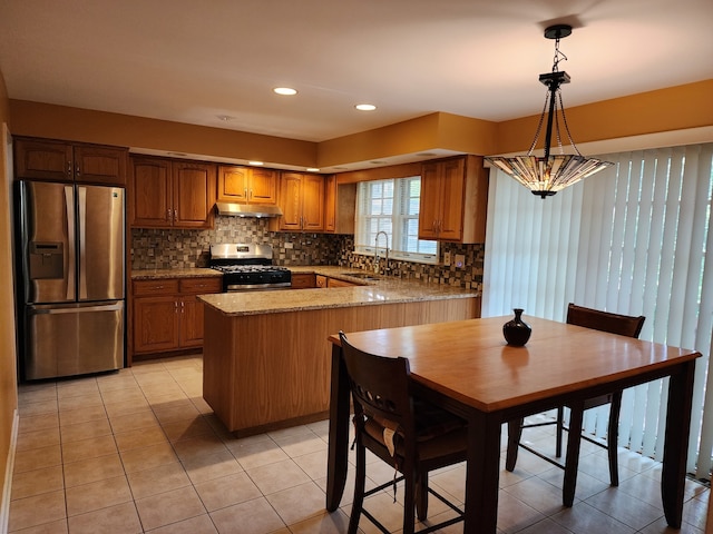 kitchen with tasteful backsplash, stainless steel appliances, hanging light fixtures, sink, and light stone counters