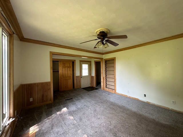 unfurnished bedroom with ceiling fan, a closet, dark colored carpet, and crown molding