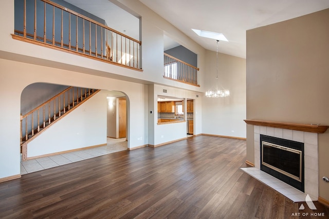 unfurnished living room featuring a tile fireplace, an inviting chandelier, hardwood / wood-style flooring, and high vaulted ceiling