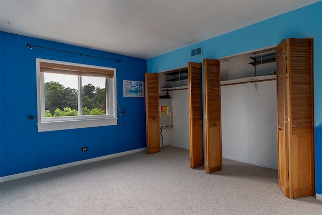 unfurnished bedroom featuring two closets, electric water heater, and light colored carpet