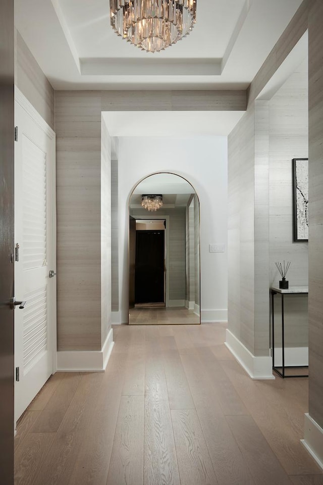 corridor with wood-type flooring, a notable chandelier, and a tray ceiling