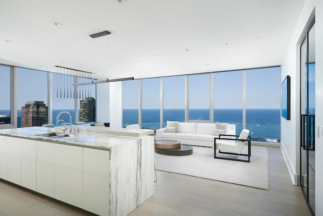 kitchen with pendant lighting, sink, white cabinetry, a kitchen island with sink, and a water view