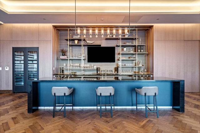 bar featuring dark parquet floors, wood walls, and hanging light fixtures