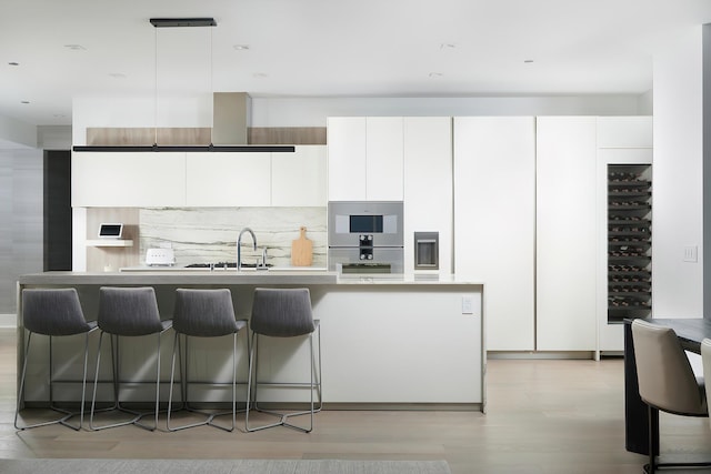 kitchen with pendant lighting, a kitchen breakfast bar, white cabinetry, and an island with sink