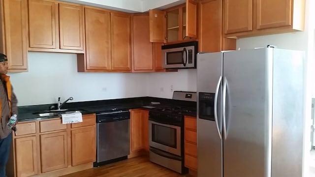 kitchen featuring light wood finished floors, brown cabinetry, dark countertops, appliances with stainless steel finishes, and a sink