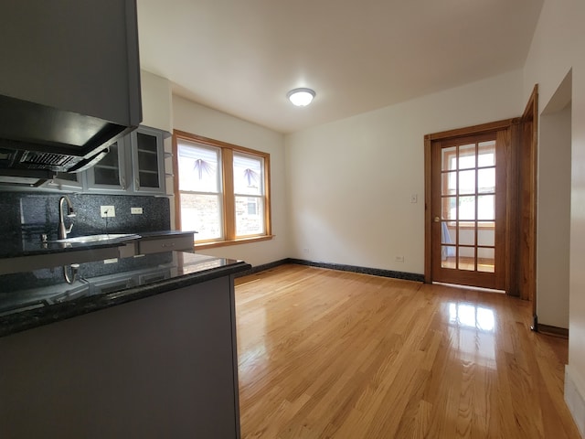 kitchen featuring sink, light hardwood / wood-style flooring, backsplash, and dark stone countertops