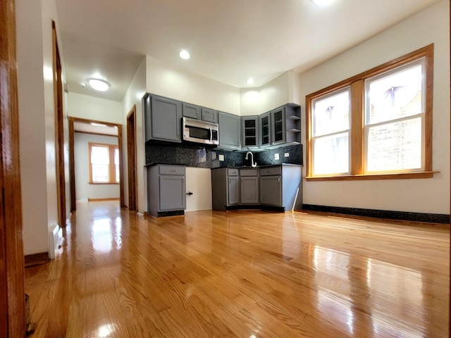 kitchen with tasteful backsplash, gray cabinets, stainless steel microwave, and light wood-style flooring