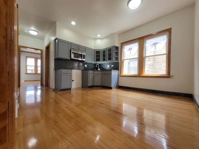 kitchen featuring gray cabinetry, baseboards, light wood-style floors, tasteful backsplash, and stainless steel microwave