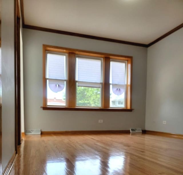 empty room with ornamental molding, visible vents, baseboards, and wood finished floors