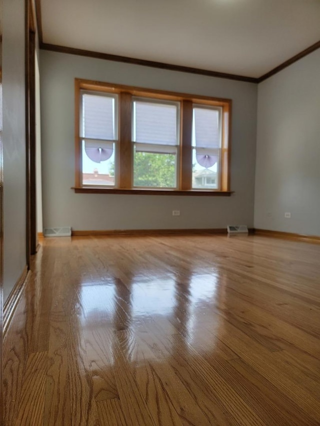 empty room with baseboards, crown molding, and wood finished floors