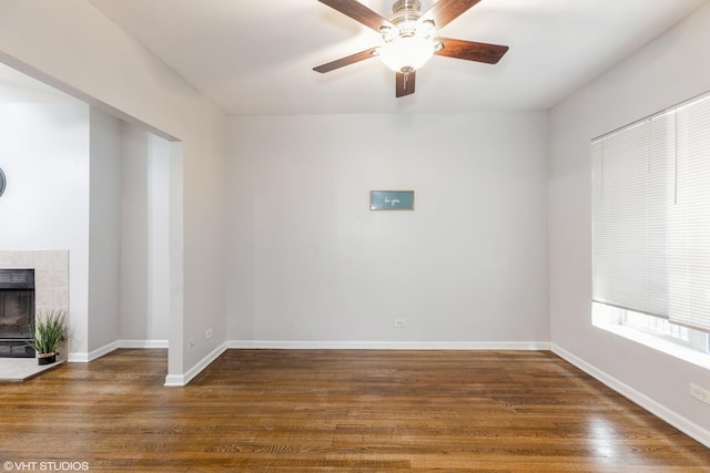 spare room with ceiling fan, baseboards, dark wood finished floors, and a tile fireplace