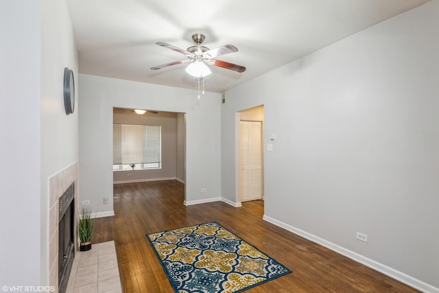 living area with a tiled fireplace, wood finished floors, a ceiling fan, and baseboards