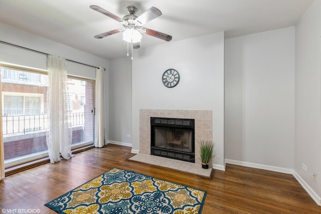 living room with ceiling fan, dark wood-type flooring, a tiled fireplace, and baseboards