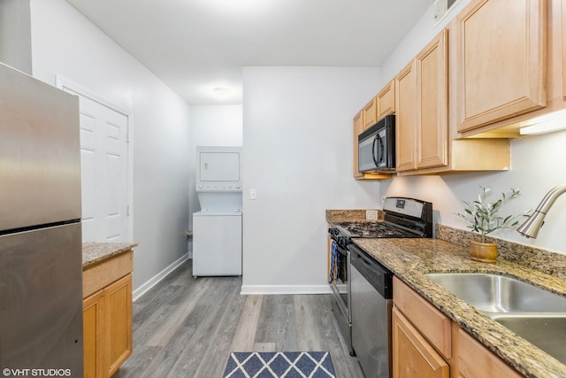 kitchen with appliances with stainless steel finishes, a sink, stacked washing maching and dryer, and light stone countertops