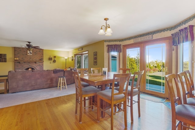 dining room with ceiling fan with notable chandelier, light hardwood / wood-style floors, and a brick fireplace