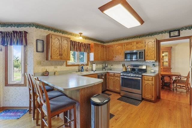 kitchen featuring kitchen peninsula, a kitchen breakfast bar, light wood-type flooring, stainless steel appliances, and sink