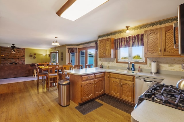 kitchen featuring pendant lighting, sink, a brick fireplace, light wood-type flooring, and kitchen peninsula