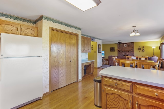 kitchen with a brick fireplace, white refrigerator, pendant lighting, ceiling fan with notable chandelier, and light wood-type flooring