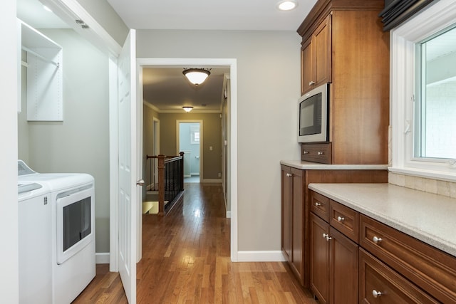 kitchen featuring stainless steel microwave, hardwood / wood-style flooring, crown molding, and washing machine and clothes dryer