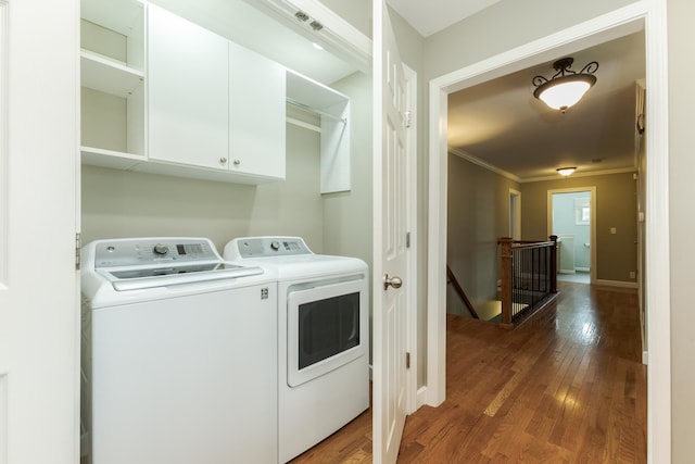 clothes washing area with washing machine and dryer, cabinets, wood-type flooring, and ornamental molding