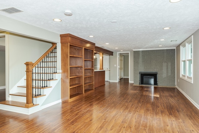 unfurnished living room featuring brick wall, a textured ceiling, a brick fireplace, and hardwood / wood-style floors