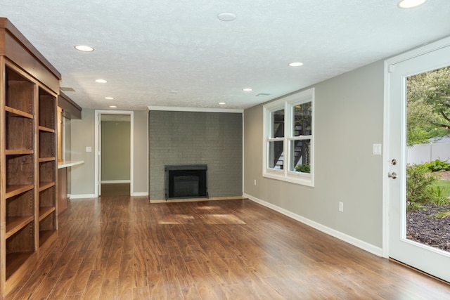 unfurnished living room with a textured ceiling, a brick fireplace, plenty of natural light, and dark wood-type flooring