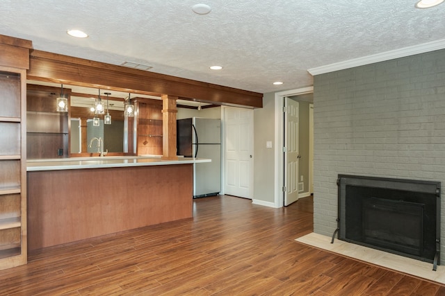 kitchen with stainless steel refrigerator, a textured ceiling, pendant lighting, a fireplace, and wood-type flooring