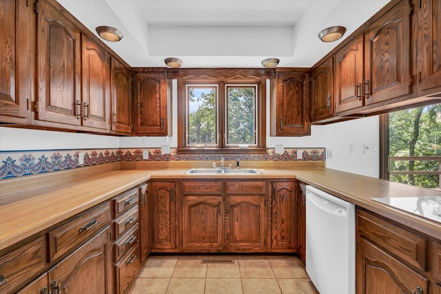 kitchen featuring cooktop, a tray ceiling, sink, dishwasher, and light tile patterned floors