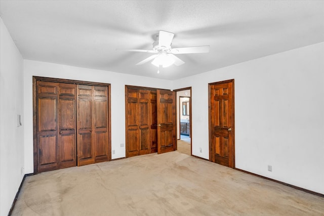 unfurnished bedroom with two closets, ceiling fan, and light colored carpet