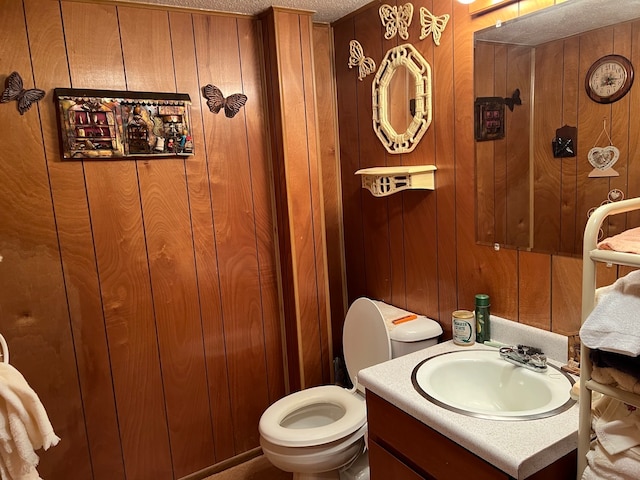 bathroom with vanity, wooden walls, toilet, and a textured ceiling