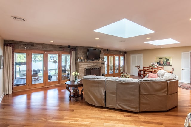 living room with light wood-type flooring, a skylight, and a brick fireplace