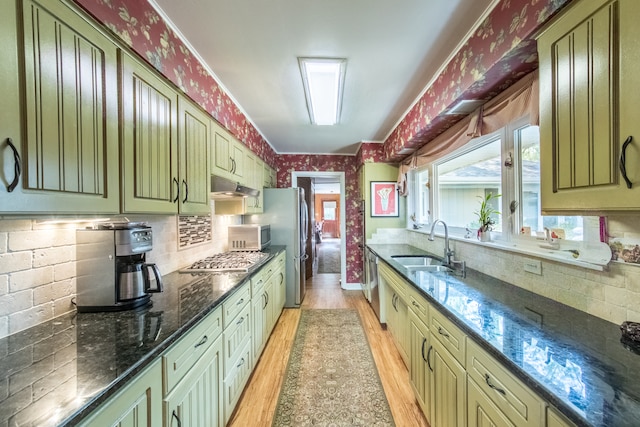 kitchen with light hardwood / wood-style flooring, appliances with stainless steel finishes, tasteful backsplash, sink, and dark stone countertops