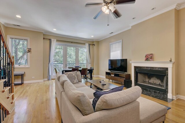 living room featuring plenty of natural light, a premium fireplace, light wood-type flooring, and ceiling fan