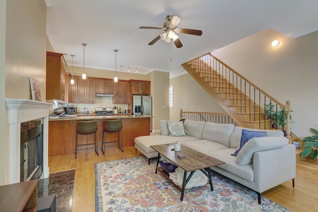 living room with a premium fireplace, light hardwood / wood-style floors, ornamental molding, and ceiling fan