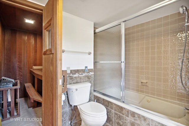 bathroom with tile patterned flooring, bath / shower combo with glass door, and toilet