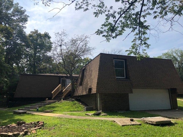 view of side of property with a garage, driveway, mansard roof, roof with shingles, and brick siding