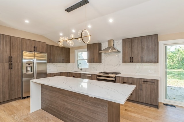 kitchen featuring plenty of natural light, vaulted ceiling, a kitchen island, wall chimney range hood, and appliances with stainless steel finishes