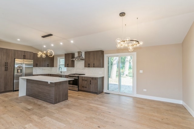 kitchen with hanging light fixtures, a kitchen island, stainless steel appliances, lofted ceiling, and wall chimney range hood