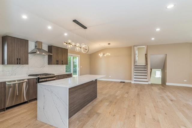 kitchen featuring pendant lighting, a kitchen island, wall chimney range hood, stainless steel appliances, and a notable chandelier